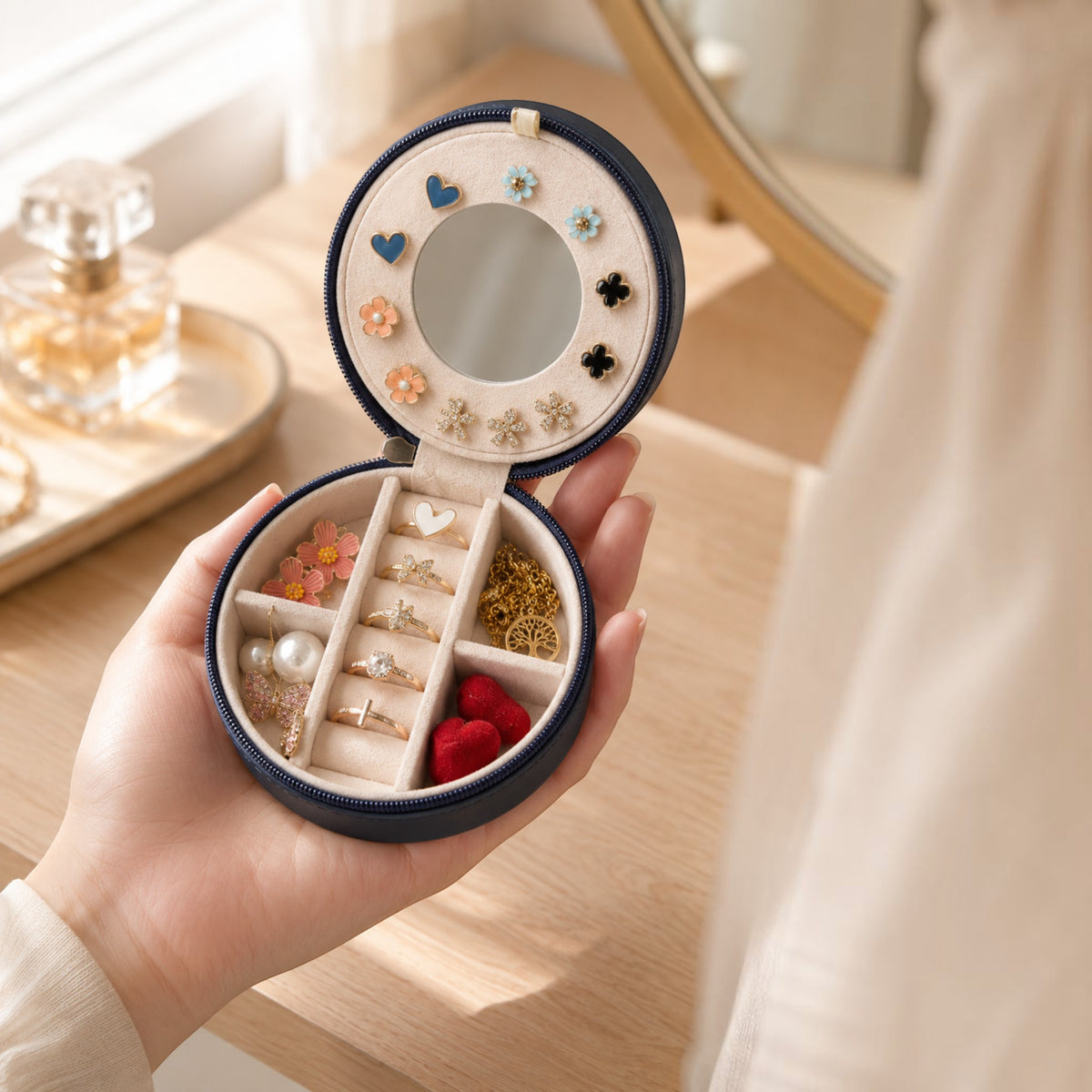 Boîte à bijoux ronde de voyage ouverte dans une main, miroir et compartiments visibles, format qui tient dans la paume